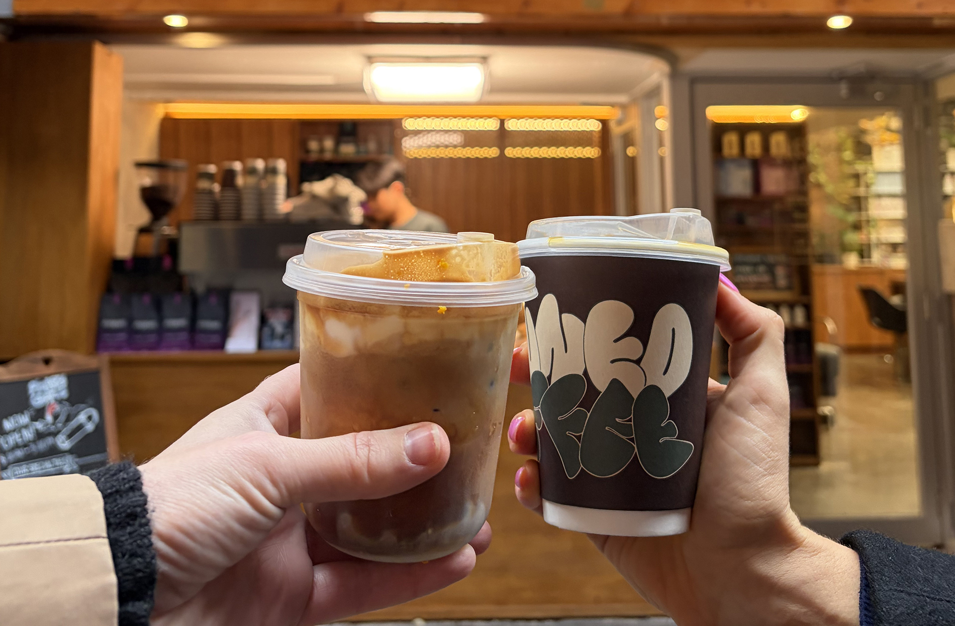Two coffees an iced and a hot being held in front of a coffee window.