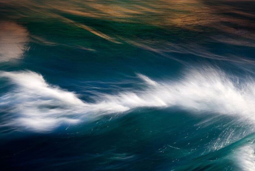 Waves in the sea with white spray on top of the breaking wave.
