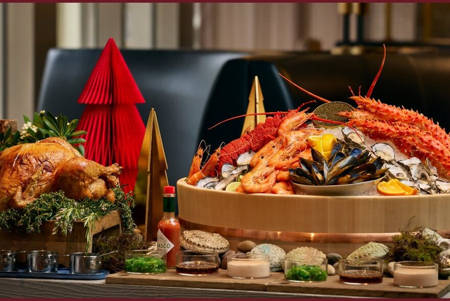 An abundant platter of seafood including prawns, lobster, oysters and mussels on a festive Christmas buffet table, a roast turkey to the left of the image.