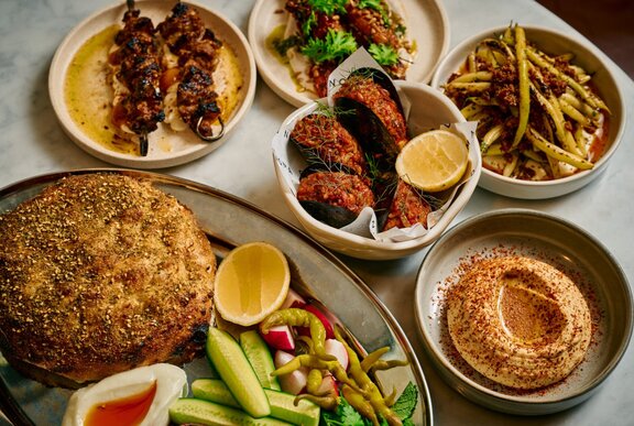 Plates of Middle Eastern food as part of a mezze lunch spread, on a restaurant dining table.