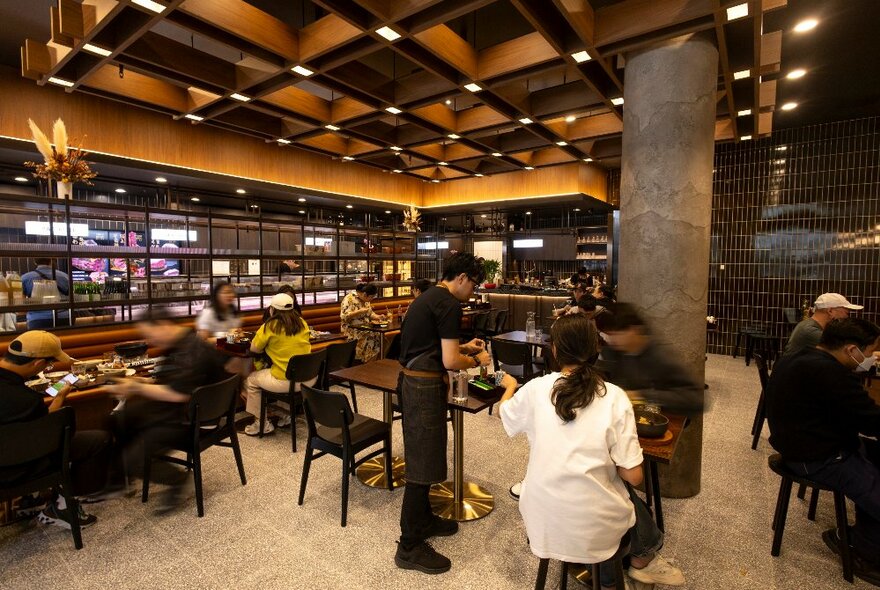 Interior of a restaurant with diners seated at tables and a glowing bar space in the background. 