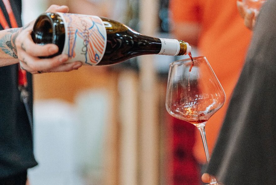 A hand holding a bottle of wine and pouring it into a glass.