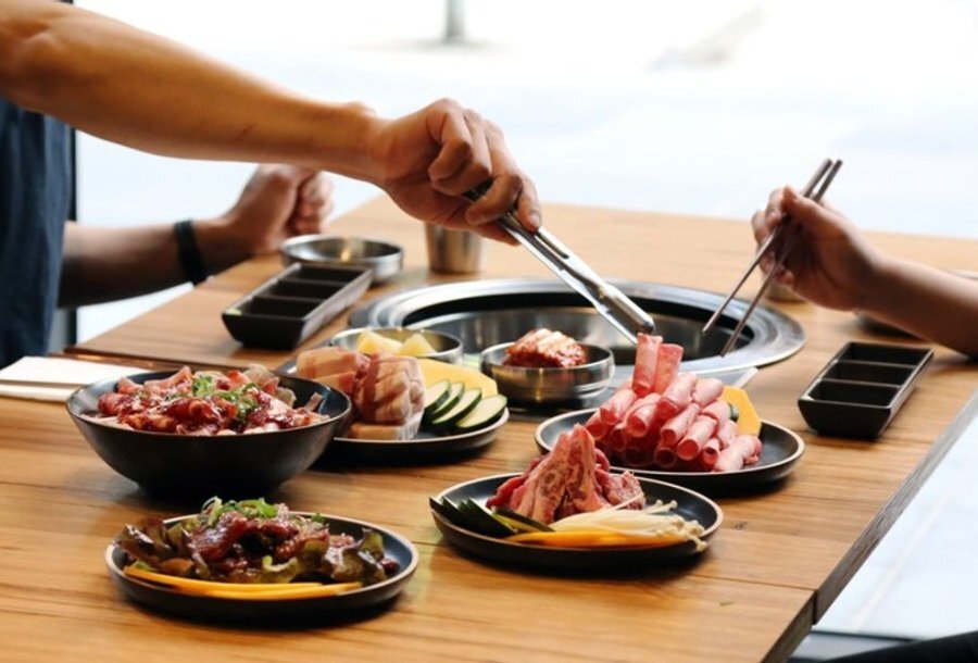 Two people with tongs picking meat up off a hot plate.
