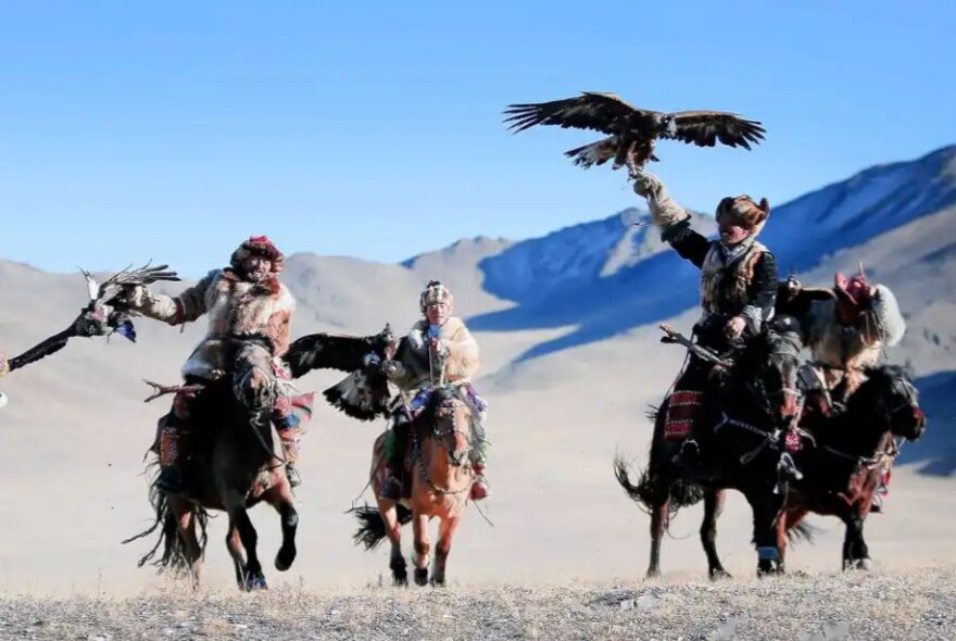 Mongolian horsemen in the desert with hunting birds.