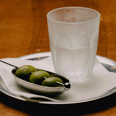 A frozen piccolo glass holding an ice-cold martini served alongside a small silver dish of green olives on a pick.