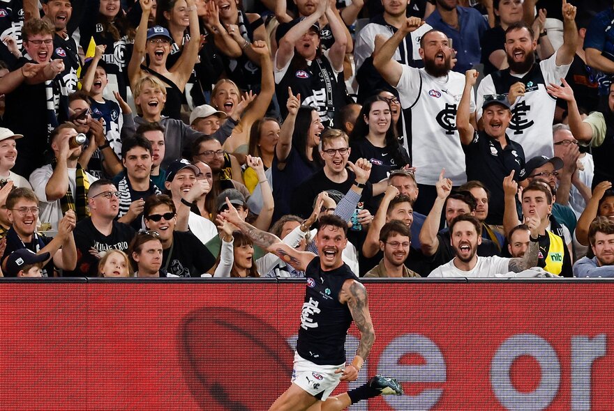 A Carlton player celebrating on field in front a packed crowd. 