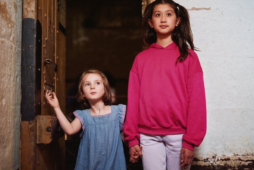 Two young girls, one small and one tall, holding hands inside the Old Melbourne Gaol.