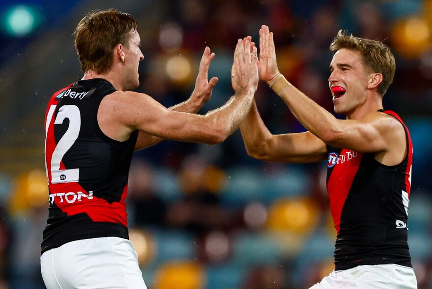 Two Essendon AFL players high fiving each other, in side profile, on the footy field.