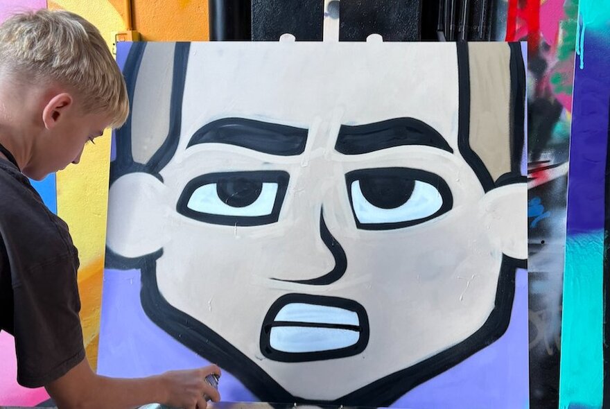 Child using spray paint to create a large cartoon artwork.