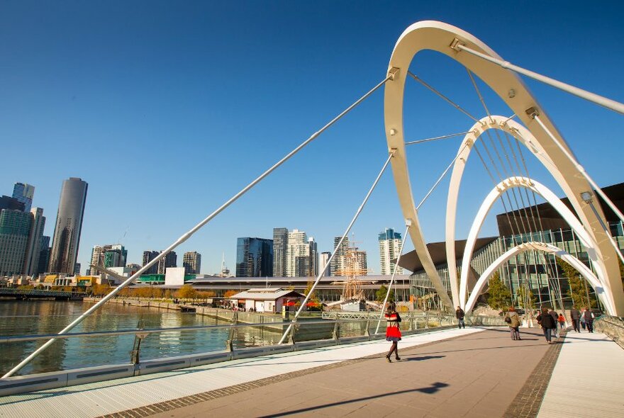 A pedestrian walking across a footbridge that features large white arches overhead.