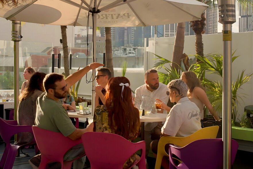 A group of people sitting around a table under a large umbrella at a rooftop bar.