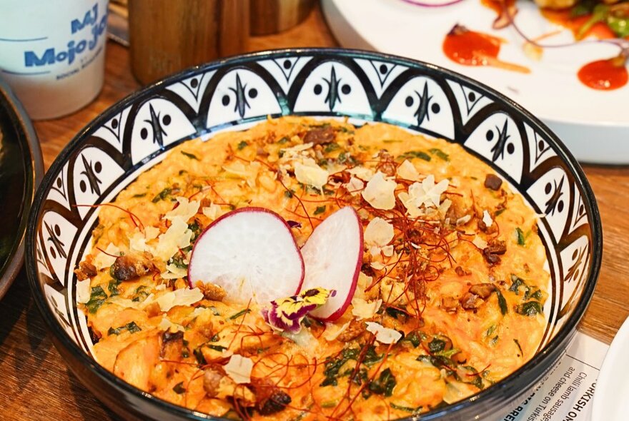 A shallow bowl of food, on a wooden cafe table.
