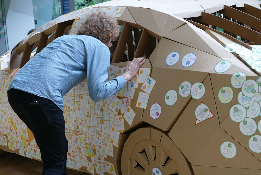 An adult peering inside The Big (Safe) Cardboard Car, a life-size educational car installation at the Melbourne Museum.