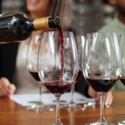 Red wine being poured from the bottle into a row of wine glasses on a table.