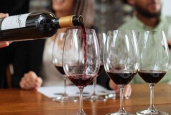 Red wine being poured from the bottle into a row of wine glasses on a table.