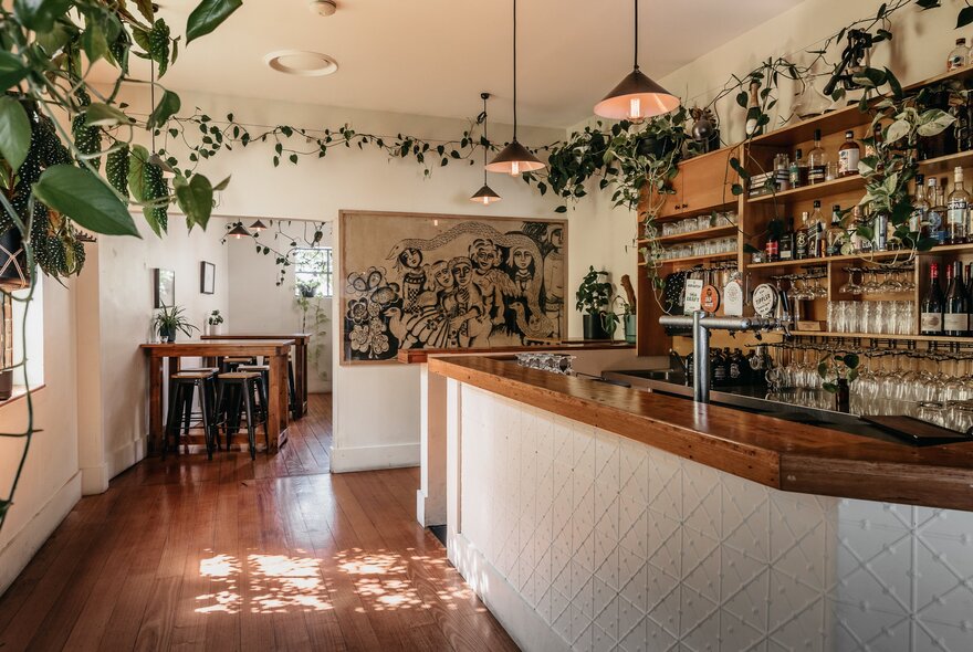 Bar area in a bistro with climbing plants stretching along one line, pendant lights over wooden counter.