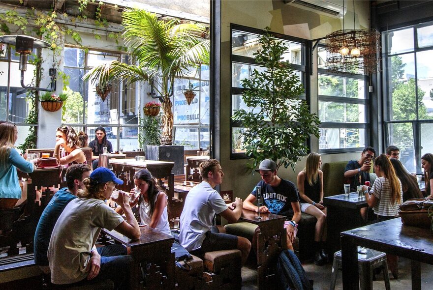 Interior of bar showing with people seated at small tables and windows overlooking the street.