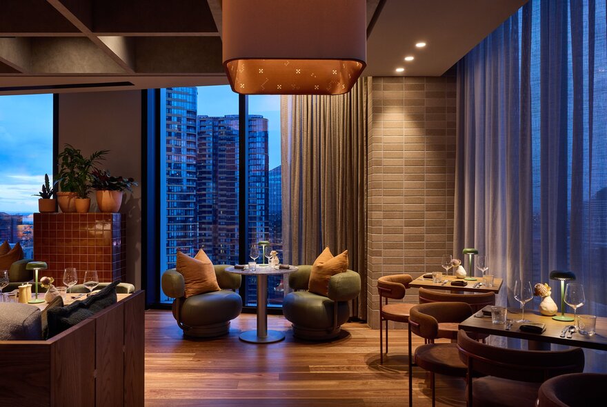 A view of a table with two plush armchairs inside the Langlands restaurant, with Melbourne's skyline visible through the tall windows.