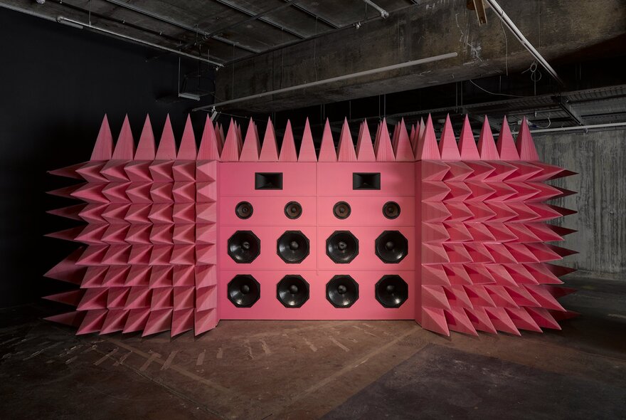 A large pink spiky wall of speakers in an exhibition space. 