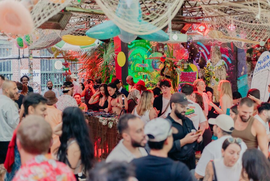Revellers at an open-air Melbourne bar with bright colours painted on the wall and netting hanging from the roof.