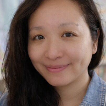 Author Angie Cui, with long dark hair, shelves of children's books in the background.