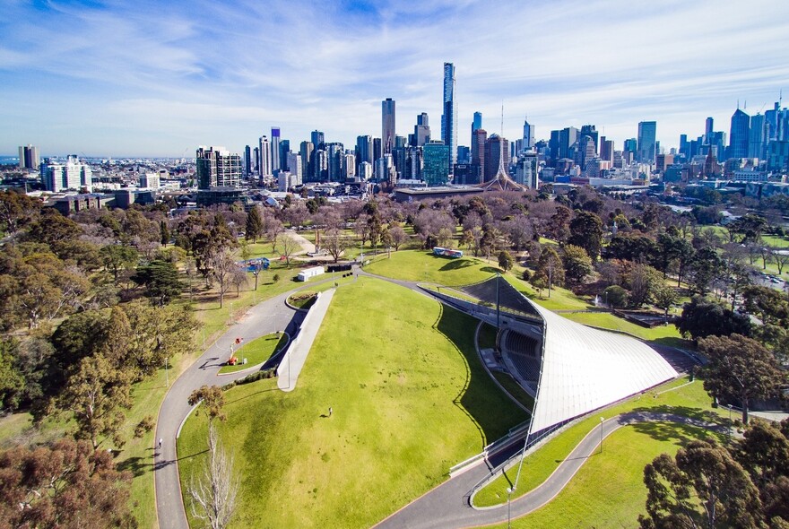 Aerial view of Sidney Myer Music Bowl showing open grassy area, covered stage and city beyond.