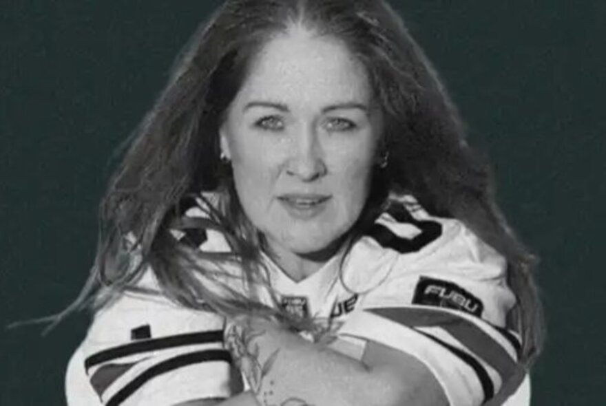 Woman with long dark hair, seated looking forward with arms crossed.