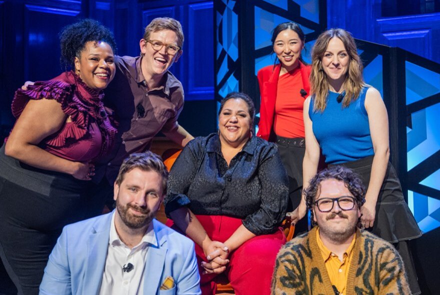 A group of seven smiling comedians on a stage as part of the The Annual Great Debate.