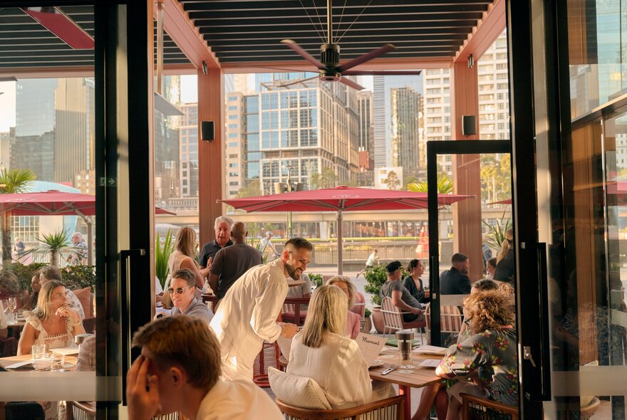 Patrons seated at a restaurant looking out over the Yarra River, with Melbourne's city buildings seen through the window.