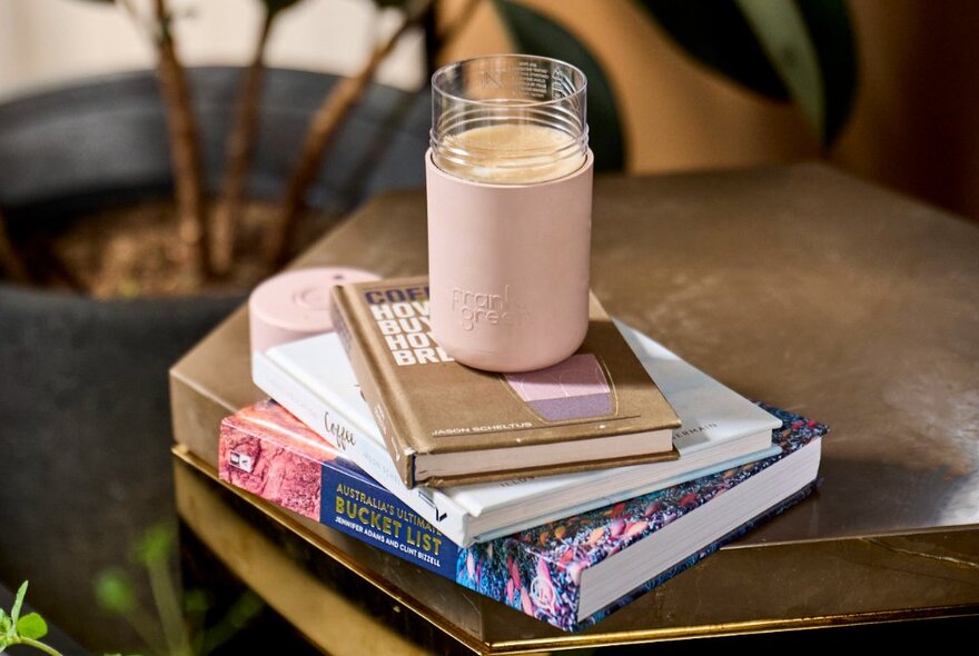 A keep cup on top of a pile of coffee table books. 