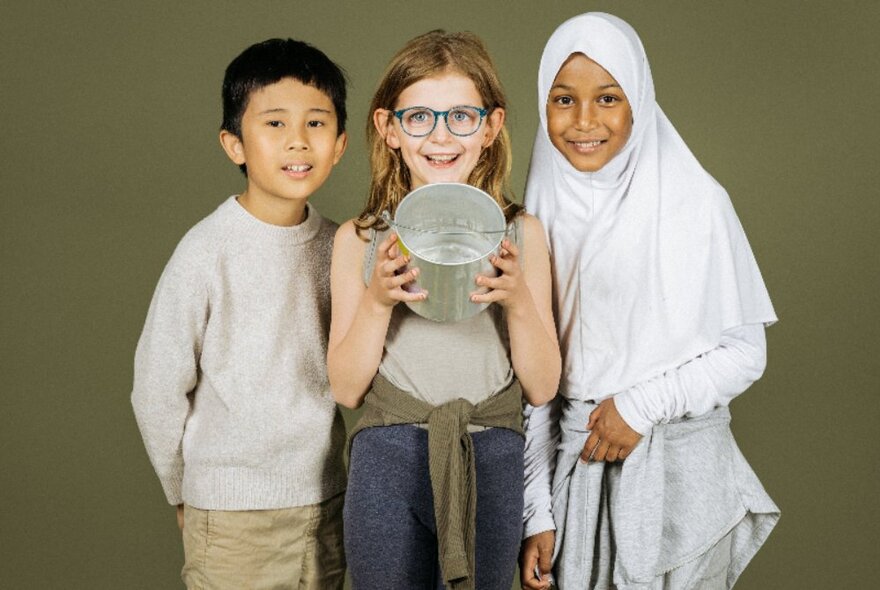 A group of three young kids huddled together smiling, the middle child holding forth an empty tin.