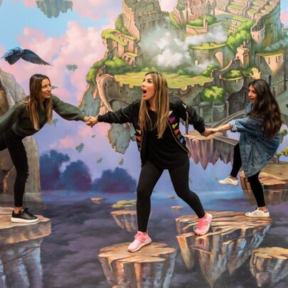 Three women joining hands and fooling around in a hand-painted interactive artwork of a fantasy landscape at ArtVo.