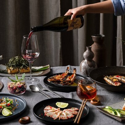 A person pouring red wine into a wine glass on a table with a variety of dishes including seafood, salads and desserts.