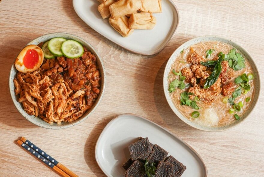 Dishes of Asian food on a table with chopsticks, including soup and stirfry.
