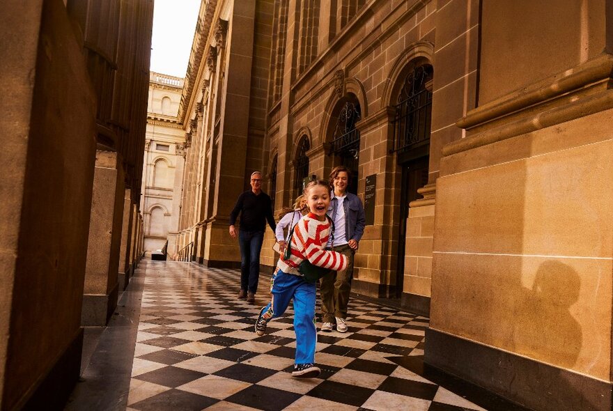 Children with family running down tiled corridor in State Library portico.