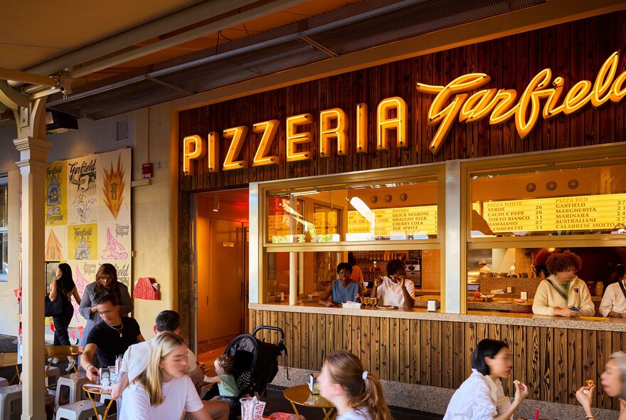 People sitting outside an Italian pizzeria with seating in the windows.