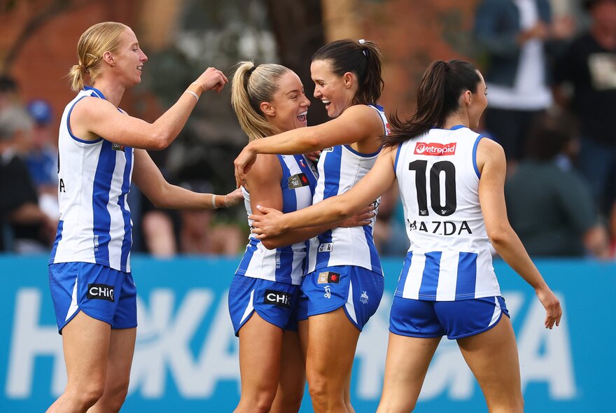 Players from the North Melbourne Kangaroos celebrating a goal during an AFLW match.