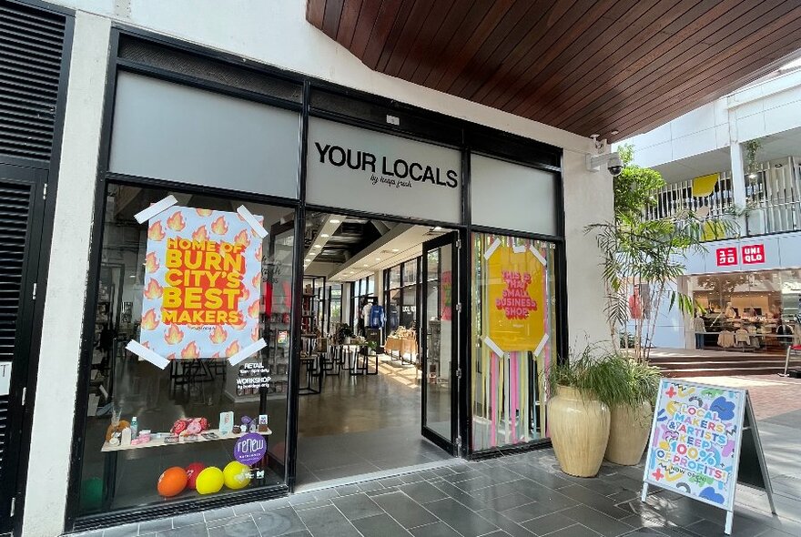 Exterior of the shop Your Locals in Docklands showing paved entrance and large glass windows and door.