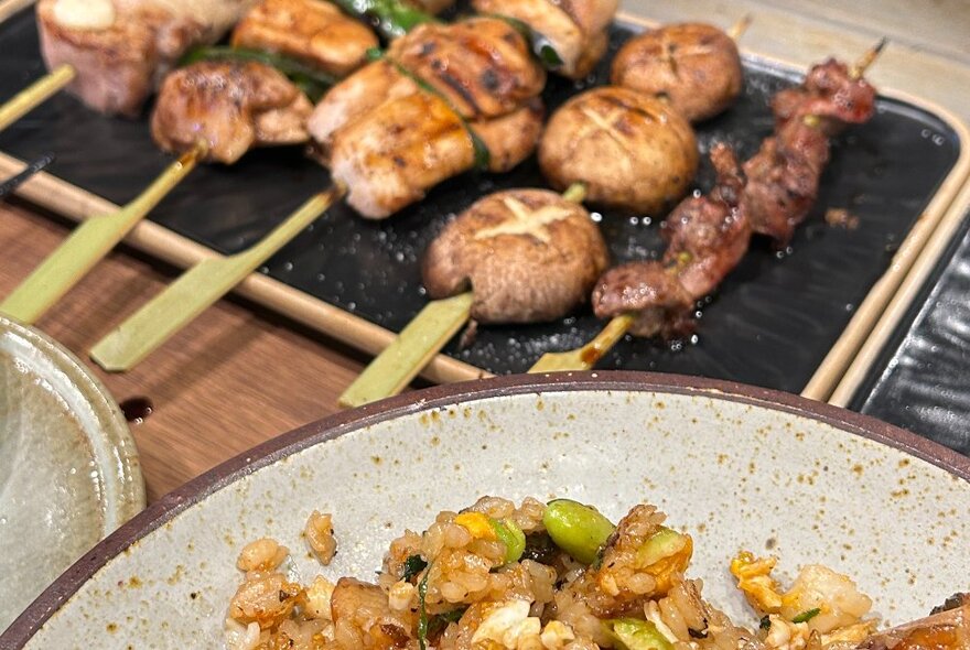 Skewers of meat next to a portion of a bowl of rice.