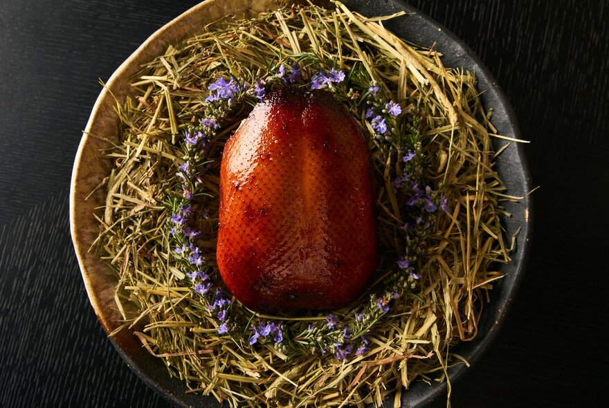 Glazed roasted duck served on a plate surrounded by small delicate flowers.