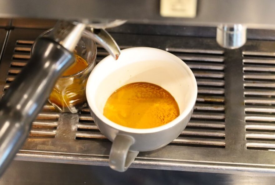 Close up of a coffee machine showing coffee dripping into a cup and a glass.
