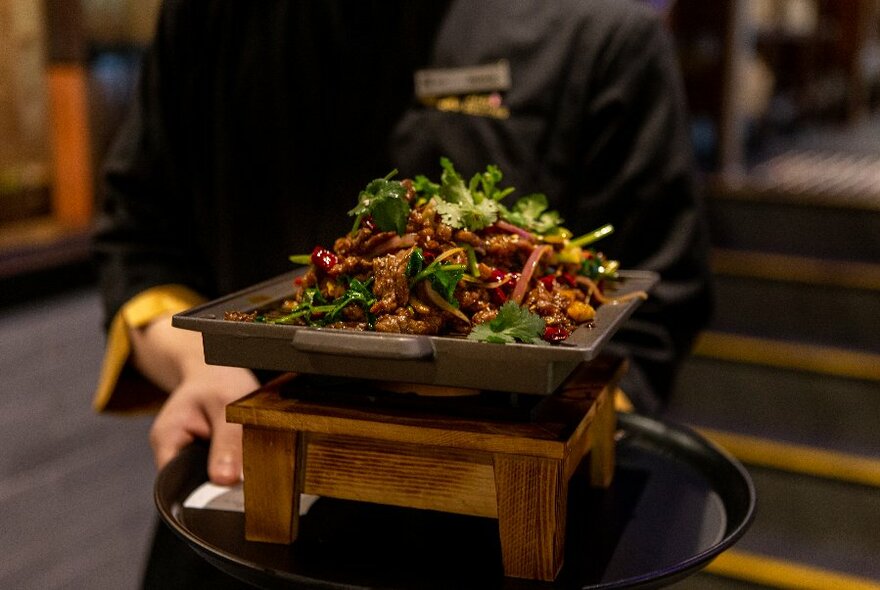 Person serving a Chinese meal on a hotplate, with small wooden stand under the hotplate.