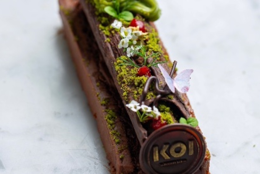 A chocolate dessert bar in the shape of a log with almond, matcha, and raspberry decoration.