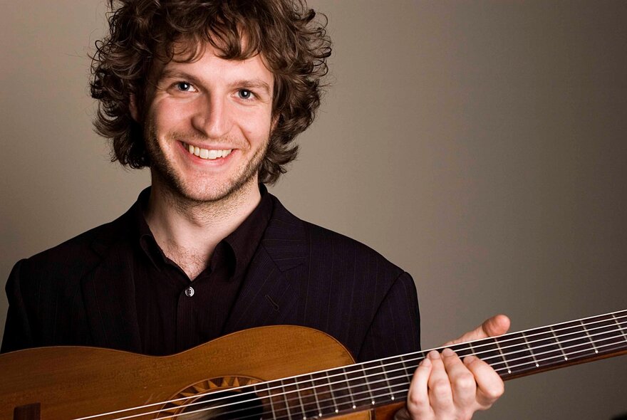 Classical guitarist Rupert Boyd smiling at the camera, with thick curly brown hair framing his face.