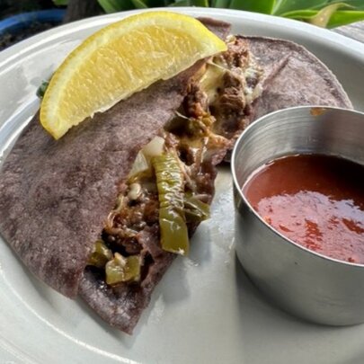 A plate with a quesadilla and cup of salsa on it.