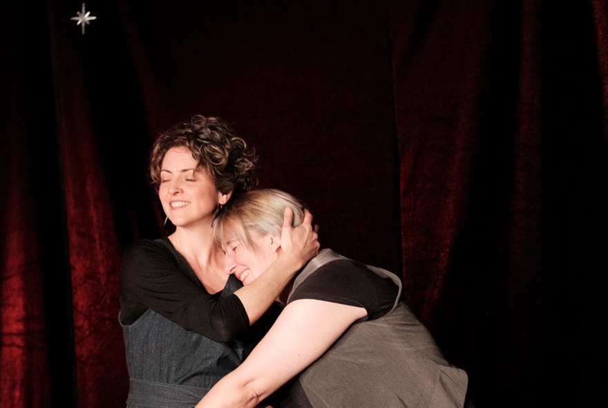 Two actors improvising live on a theatre stage in front of a black curtain.