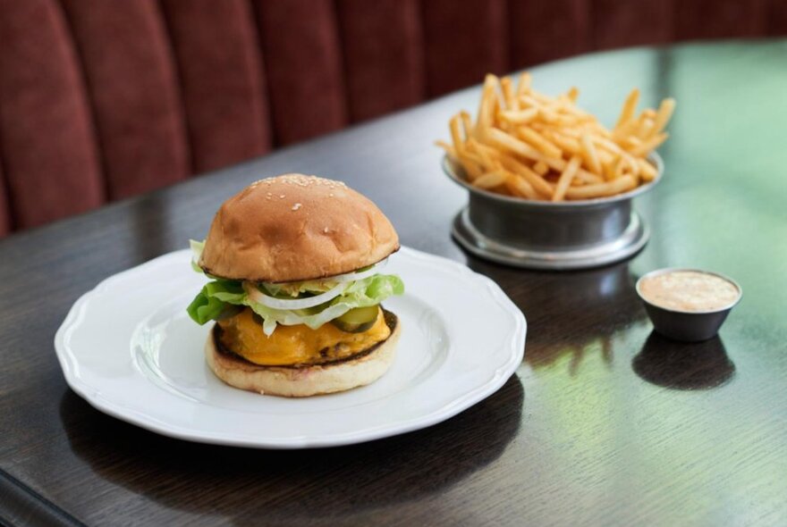 Burger on a white plate with fries and sauce.