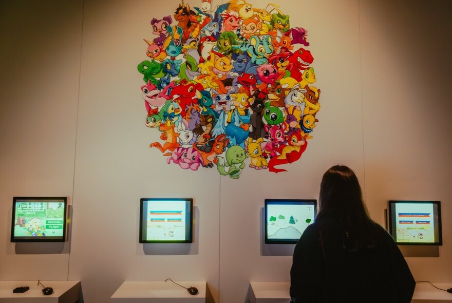 The back of a person who is interacting with screens fixed to a wall as part of an exhibition on display at ACMI.