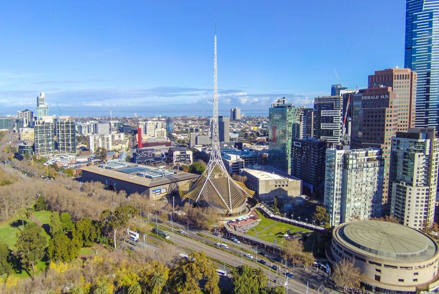Arts Centre Melbourne with winter trees and blue sky, surrounded by city buildings.
