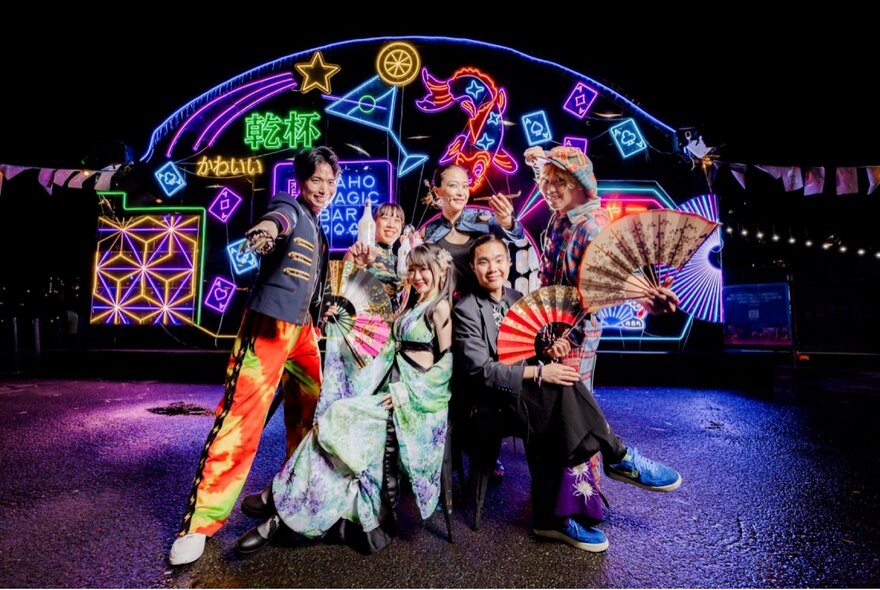 A group of people posing for a photo in front a neon lit backdrop at night.